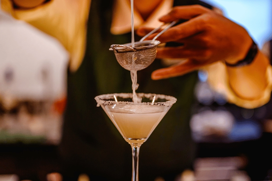 bartender making a craft cocktail in a martini glass and using a strainer